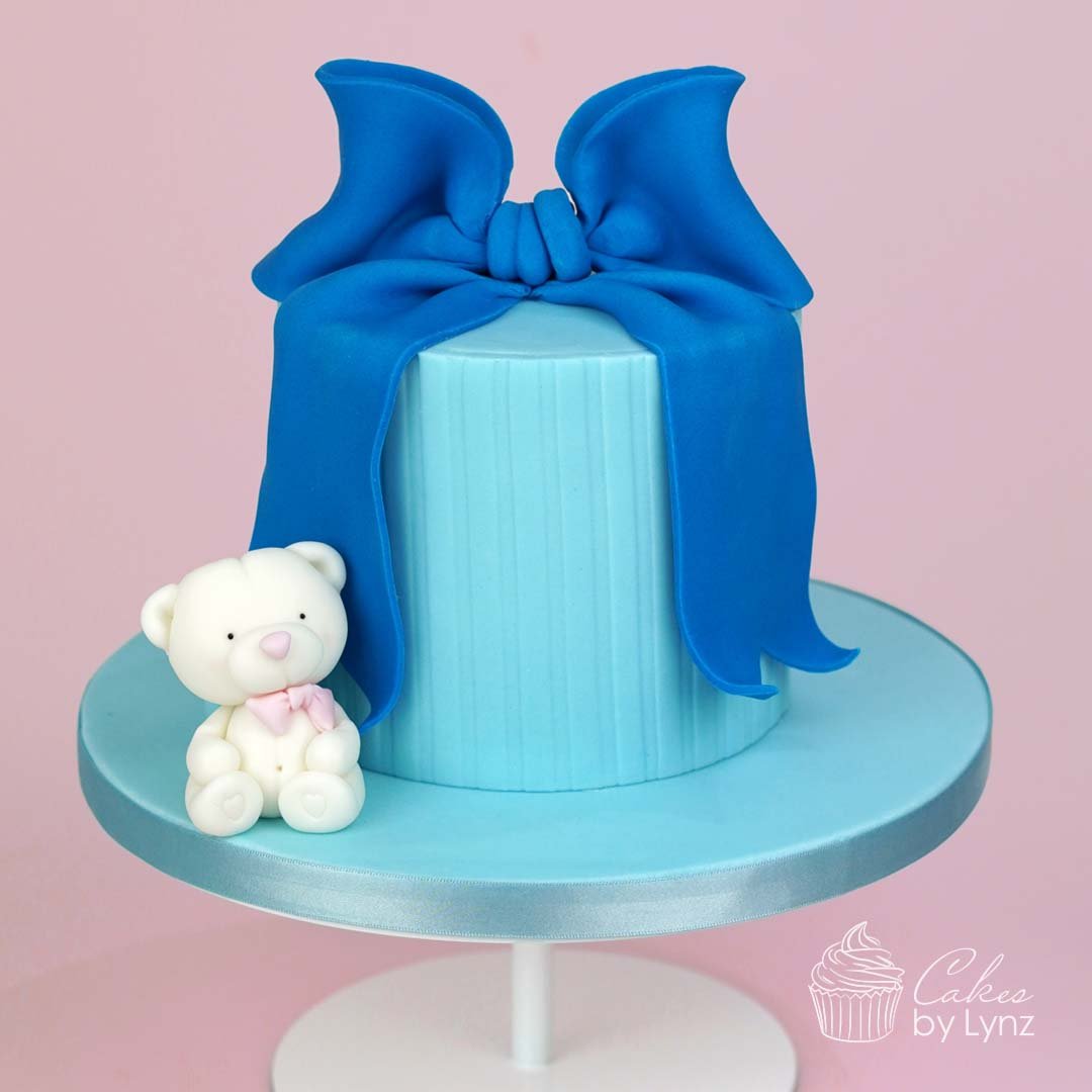 teddy bear cake topper sitting on a blue bow cake tutorial